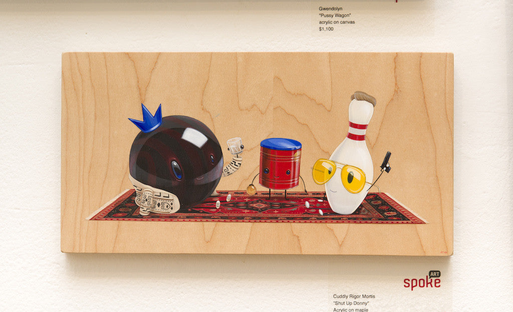 A whimsical Cuddly Rigor Mortis illustration features a bowling ball with a blue crown and dollar bills, a small red drum, and a pin in yellow glasses on wood, coming to life like an acrylic painting on maple over a decorative rug design.