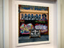 A framed painting by Jessica Hess depicts a vibrant graffiti street scene with colorful letters and a large face on a cart. Monochrome portraits adorn the top windows, while a No Parking! sign punctuates the lively urban canvas.