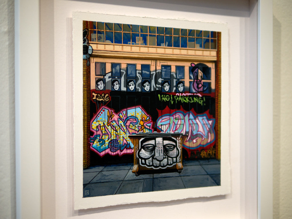 A framed painting by Jessica Hess depicts a vibrant graffiti street scene with colorful letters and a large face on a cart. Monochrome portraits adorn the top windows, while a No Parking! sign punctuates the lively urban canvas.
