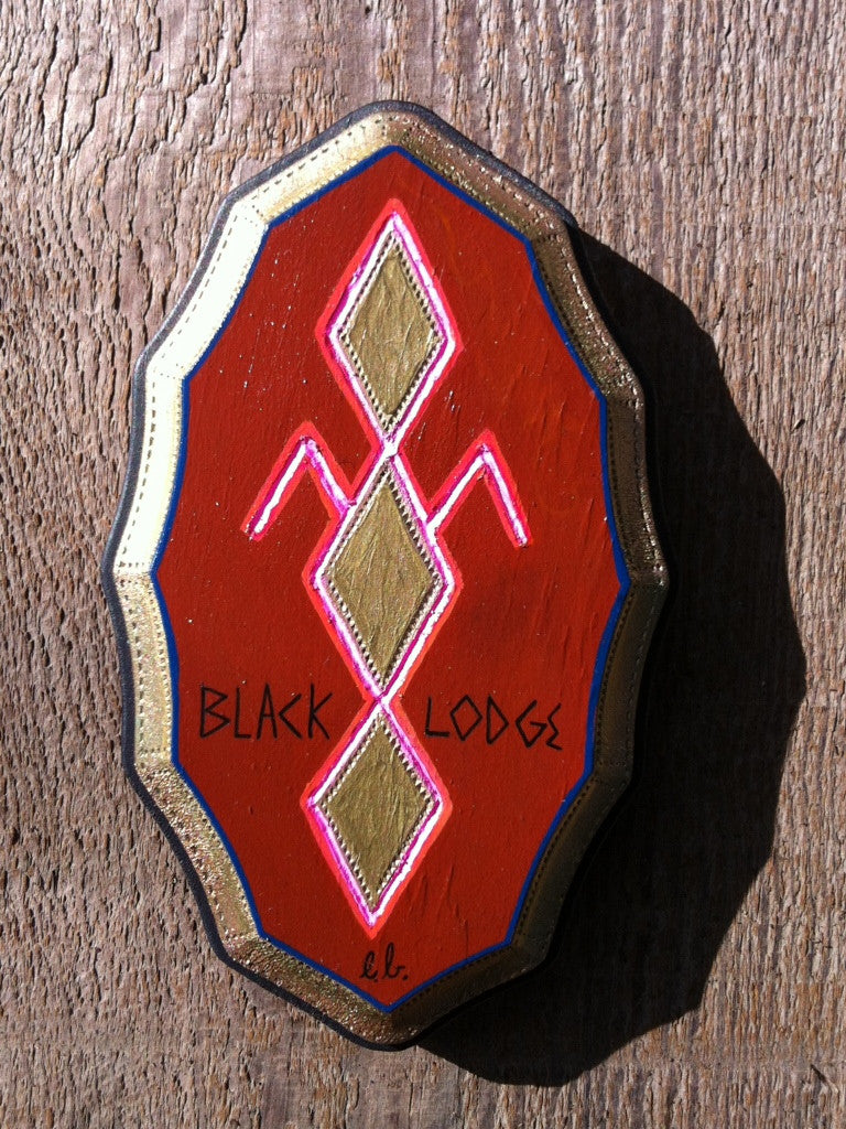 A red emblem displays gold and pink diamond motifs and lines, with the text Black Lodge by Evan Harris artistically inscribed below, all set against a luxurious wooden backdrop.