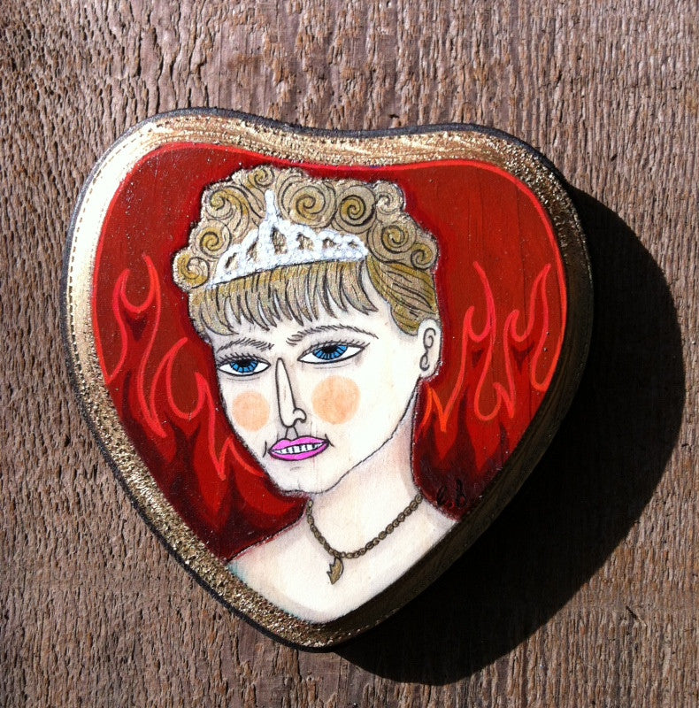 A heart-shaped mixed media artwork by Evan Harris features a portrait of a person with short, curly hair wearing a tiara. Against an abstract, red flame-like background, it is displayed on wood at Spoke Art Gallery.
