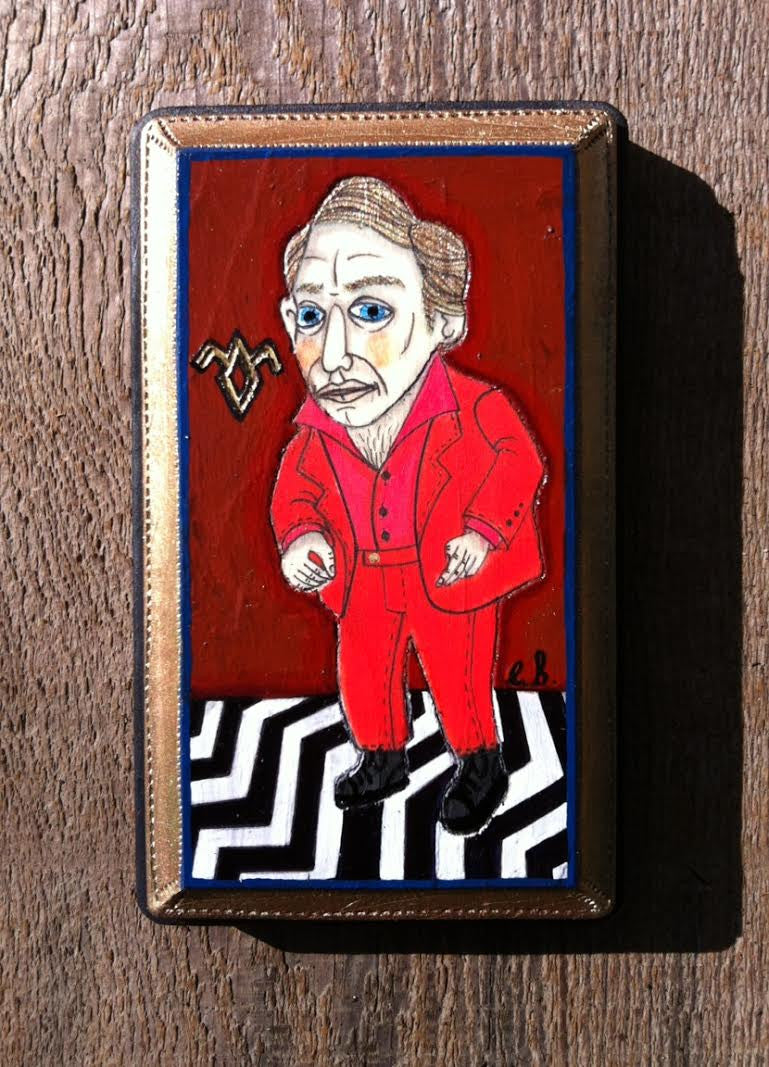 A stylized mixed media painting by Evan Harris depicts a man in a red suit with blue eyes on a zigzag black-and-white floor, against a deep red background featuring a strange symbol. It is framed in gold on wood, reminiscent of an exhibit at Spoke Art Gallery.