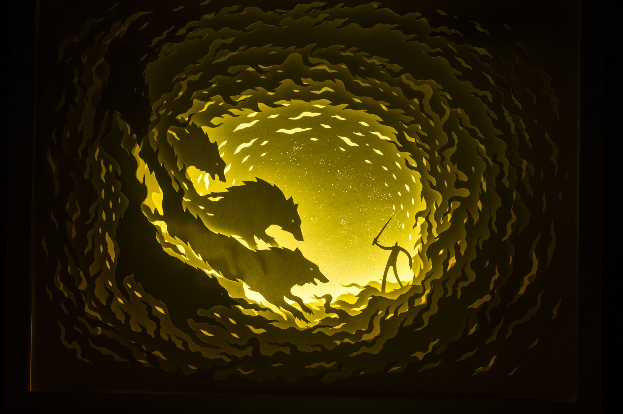 A meticulously crafted cut paper silhouette by Hari & Deepti shows three wolves on a cliff beneath a starry night. Intricate layers and swirling patterns with a yellow glow create a dramatic effect similar to Firewolves and the Lone Warrior art piece.