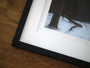 This close-up highlights a detailed giclee print of a snowy forest by Henrik Uldalen, marked 17/75. It is preserved with archival framing featuring a black frame and white border, elegantly displayed on wood.