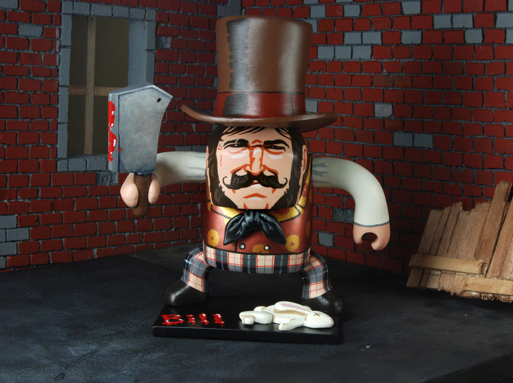 A Geoff Trapp toy figure, inspired by a Scorsese character, features a large top hat and mustache while holding a cleaver. Wearing plaid pants and a vest, it stands on a base labeled Bill in red against brick walls and wooden planks, capturing The Film Foundations cinematic style.
