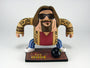 A cartoon figure of a long-haired, bearded man wearing sunglasses, a patterned sweater, and striped pants stands on a The Dude vinyl mat with a bowling ball in front. Brand: Geoff Trapp.