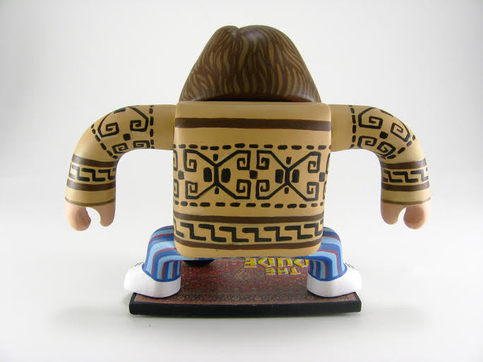 A stylized figure with long hair stands on a vinyl-like platform, wearing a tan shirt with tribal patterns and blue-striped pants. Arms are outstretched, capturing Geoff Trapps mixed media style.