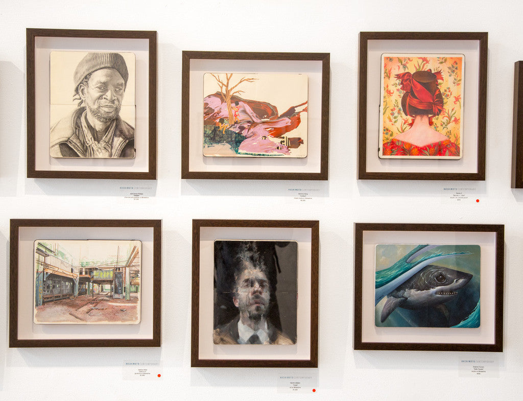 A gallery wall displays six custom-framed Jessica Hess artworks, featuring portraits, a nature scene with birds, a red-haired woman in floral setting, gouache on Moleskine of a shark underwater, and a city landscape. Each frame includes a label highlighted with a red dot below.