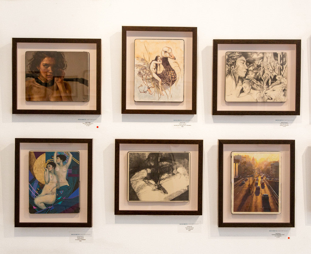 A gallery wall features six custom-framed artworks, including an exquisite Greg Gandy oil painting. The collection showcases distinct portraits and abstract designs arranged in two rows of three against a crisp white backdrop.