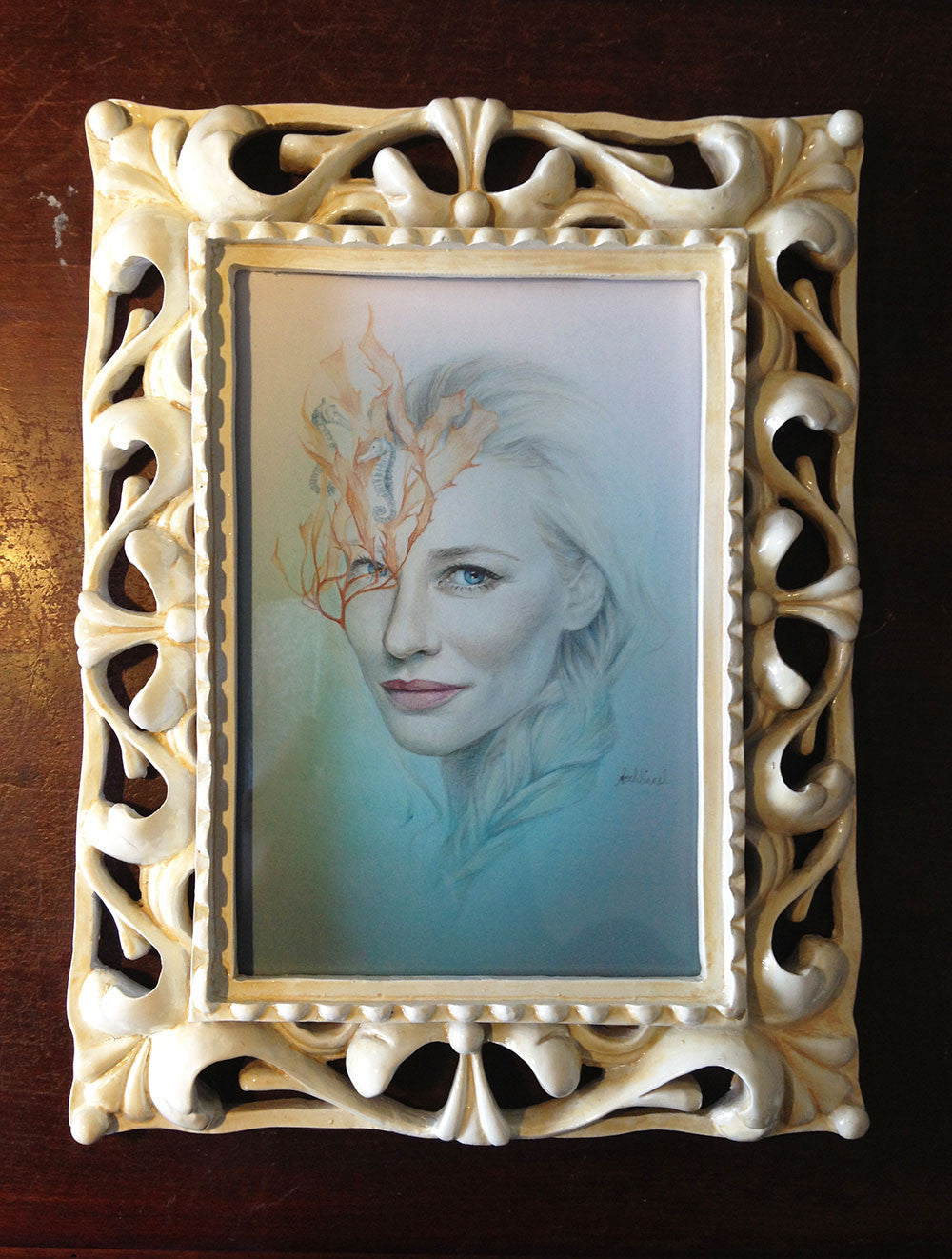 This framed artwork, by Bec Winnel, features a womans portrait with a white ornate border. The image showcases soft colors and an illustrated leaf pattern over the face, embodying the delicate detail and style reminiscent of colored pencil artistry.