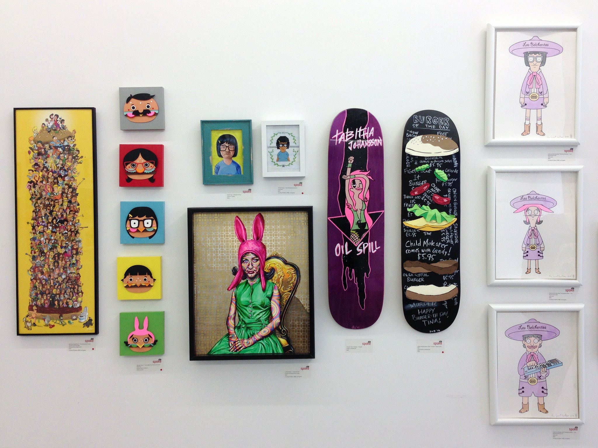 A gallery wall featuring eclectic art pieces, from framed portraits to decorated skateboards, includes vibrant highlights from The Beast Brothers. This modern and pop-art blend showcases colorful graphics and abstract designs in a visually striking composition.
