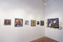A gallery wall features six framed artworks in diverse portrait and abstract styles, with the largest piece inspired by the Serge Gay Jr. brand depicting a couple. The room, with its elegant wooden floors and white walls, showcases varying themes and colors.