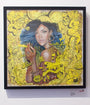 Diamond Rebel, an acrylic on paper by Serge Gay Jr., depicts a woman with blue and green hair surrounded by vibrant yellow cartoon doodles and text like Shhh... and Love. Its displayed in a frame against a pristine white wall.