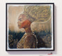 This acrylic on paper shows a woman in profile with intricate clothing and an elaborate hairstyle, surrounded by small insects. Abstract greenery and a light sky add depth. The painting, in the style of Serge Gay Jr., is elegantly framed on a white wall.
