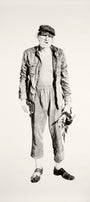 A monochromatic drawing from Joel Phillips captures an elderly man in a cap, jacket, and loose pants. Holding a small figurine and a book, his detailed posture is beautifully rendered with charcoal and graphite, reflecting the style seen at San Francisco art fairs.