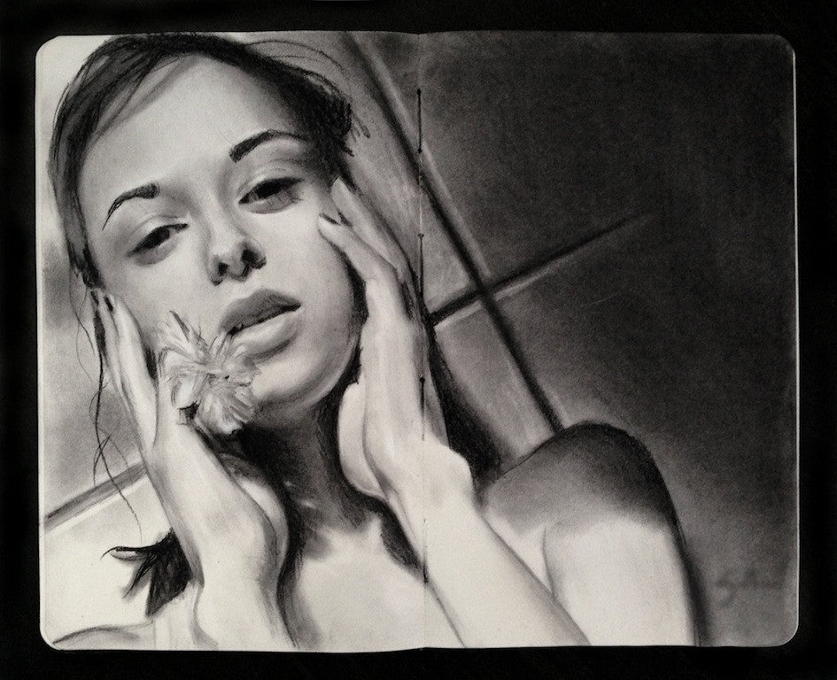 A woman touches her face, with a small flower in her right hand, her gentle gaze fixed forward against a tiled background. The artwork is Charcoal on Moleskine, capturing the evocative style associated with Kate Zambrano.