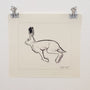A signed sketch from the Los Bocetos 11 series by Karla Ortiz, clipped to a white wall, depicts a leaping hare. The ink and graphite drawing highlights the hares detailed elongated ears and muscular form, capturing motion.