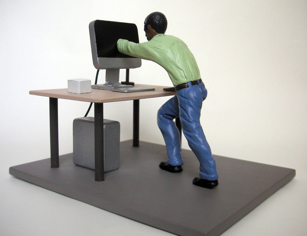 A figurine from Leon Reid IV, wearing a green shirt and blue pants, leans forward, reaching into a computer monitor. The scene, similar to setups seen at Beyond Eden Art Fair, includes a keyboard and computer tower under the desk.