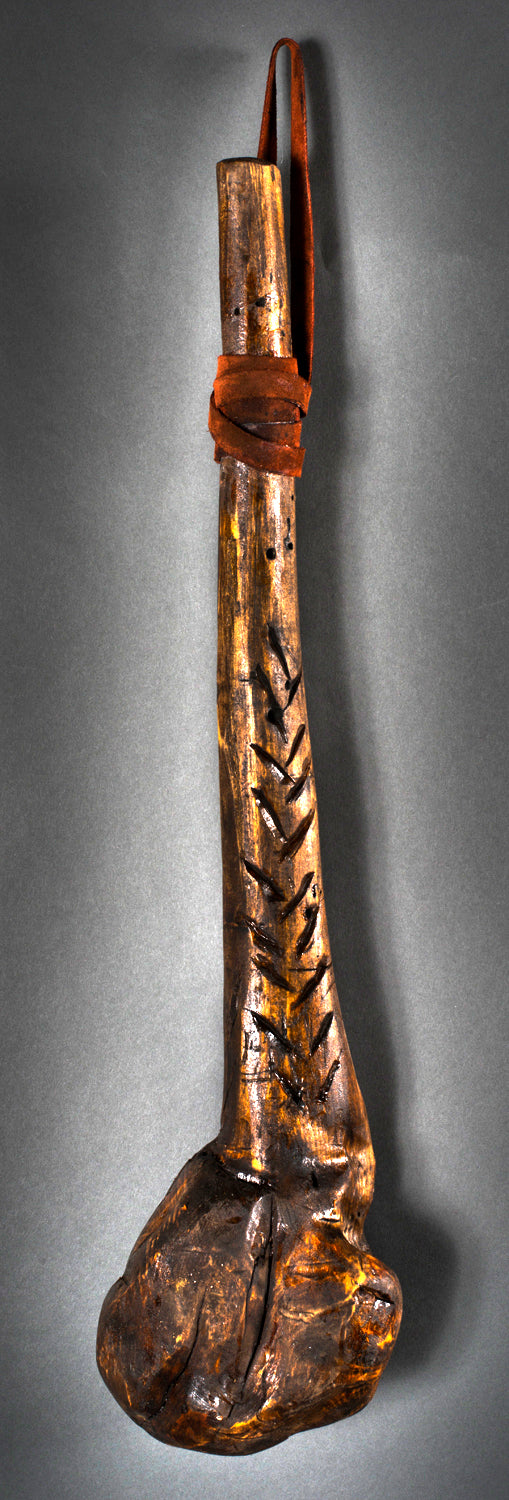 A striking handmade club by Lucien Shapiro, featuring a large rough-hewn base and slender handle, is the star of an art show. Dark wood with carved patterns and a leather strap for hanging stands against a dark background as a Martin Scorsese tribute.