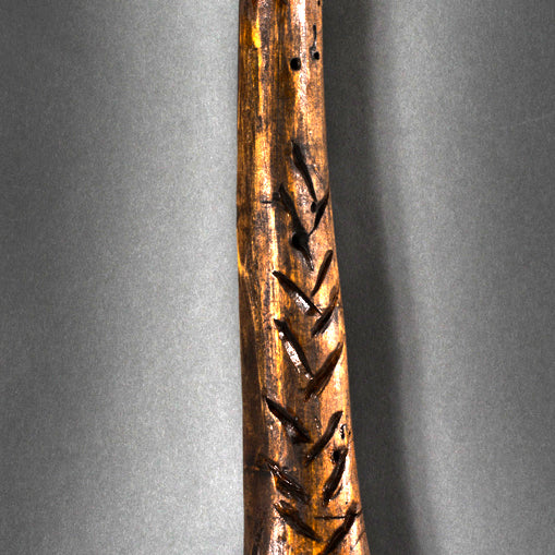 A striking handmade club by Lucien Shapiro, featuring a large rough-hewn base and slender handle, is the star of an art show. Dark wood with carved patterns and a leather strap for hanging stands against a dark background as a Martin Scorsese tribute.