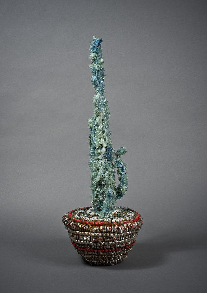 The Street Diamond Cactus Vessel by Lucien Shapiro is a tall, abstract cactus-like sculpture crafted from translucent materials in blue and green hues, set in a basket with red and metallic accents against a gray background.
