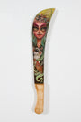 A Tatiana Suarez machete with a wooden handle features a mystical woman from Spoke Arts style. Inspired by the Mira oil series, she has green hair, a colorful headpiece, and holds a small mammal set against vibrant green and yellow hues.