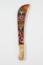 Tatiana Suarezs intricately painted machete at Spoke Art features a wooden handle and stunning blade design: a green-skinned woman with pink hair surrounded by leaves, butterflies, and a lizard, beautifully merging nature and fantasy elements.
