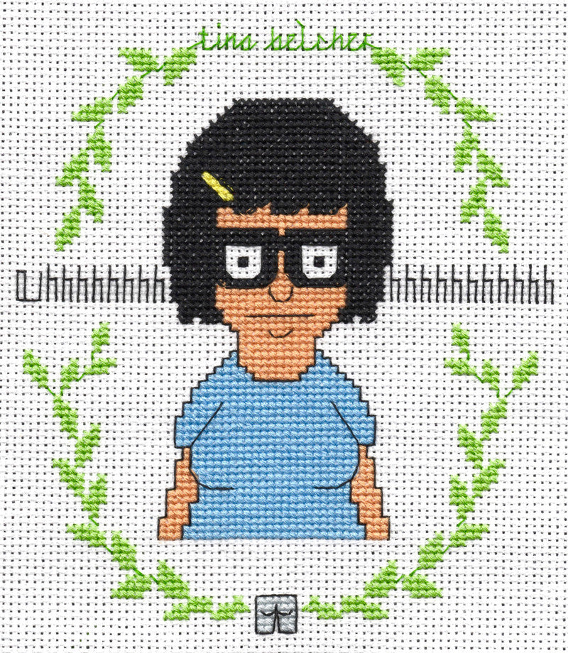 The Oh Sew Nerdy cross-stitch of Tina Belcher showcases her black hair, glasses, and blue shirt within a green leafy oval. Highlighted at the Bobs Burgers art show, it includes a gray book design for added charm.
