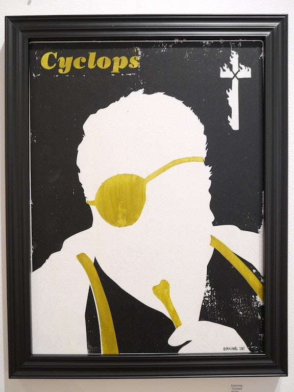 Evanimals Cyclops features a bold silhouette of a head with short hair and a yellow eye patch on a black background. Cyclops is written in yellow at the top left, with a yellow cross at the top right. This acrylic piece is beautifully framed in black.