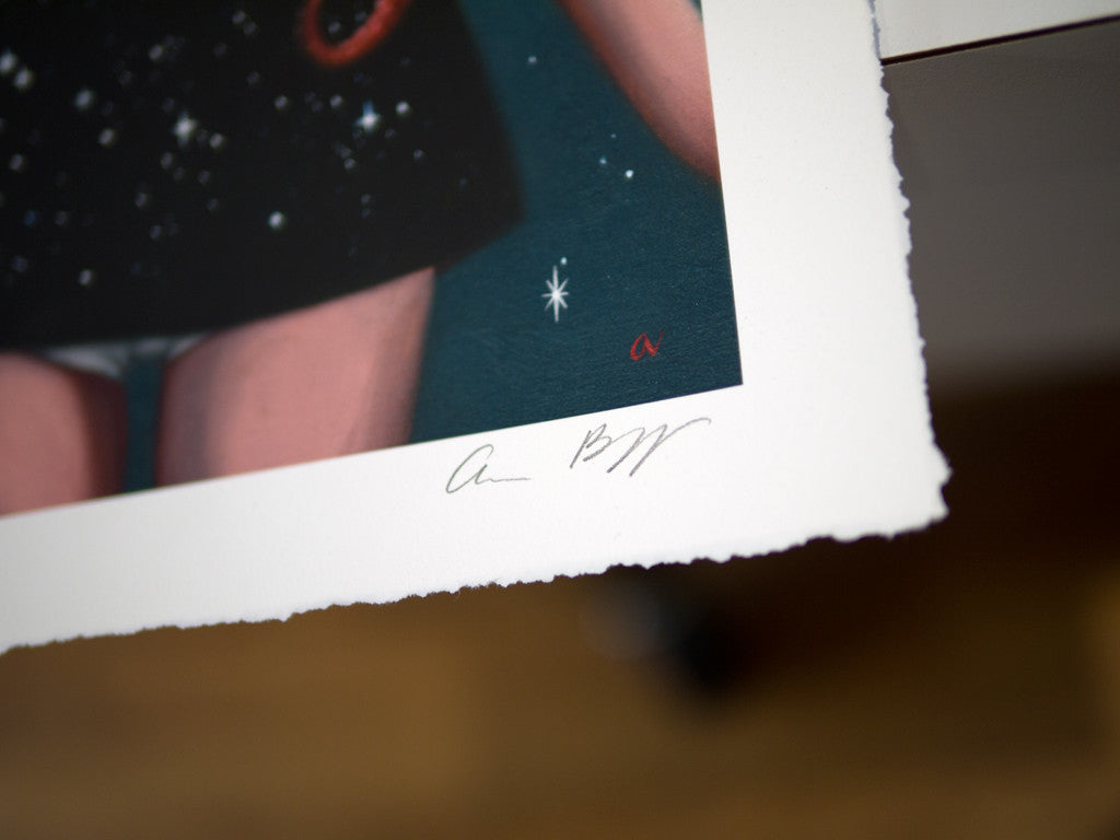 Close-up of Ana Bagayans limited edition fine art giclee print with rough edges on a table. The image shows a figure in a starry outfit, featuring Ana Bagayans white signature in the corner and another smaller red signature near the edge.