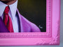 Close-up of a Scott Scheidly pink-framed fine art giclee print featuring a person in a purple suit and red tie. The frame has decorative corners, and the faint signature at the bottom right marks it as a limited edition treasure.