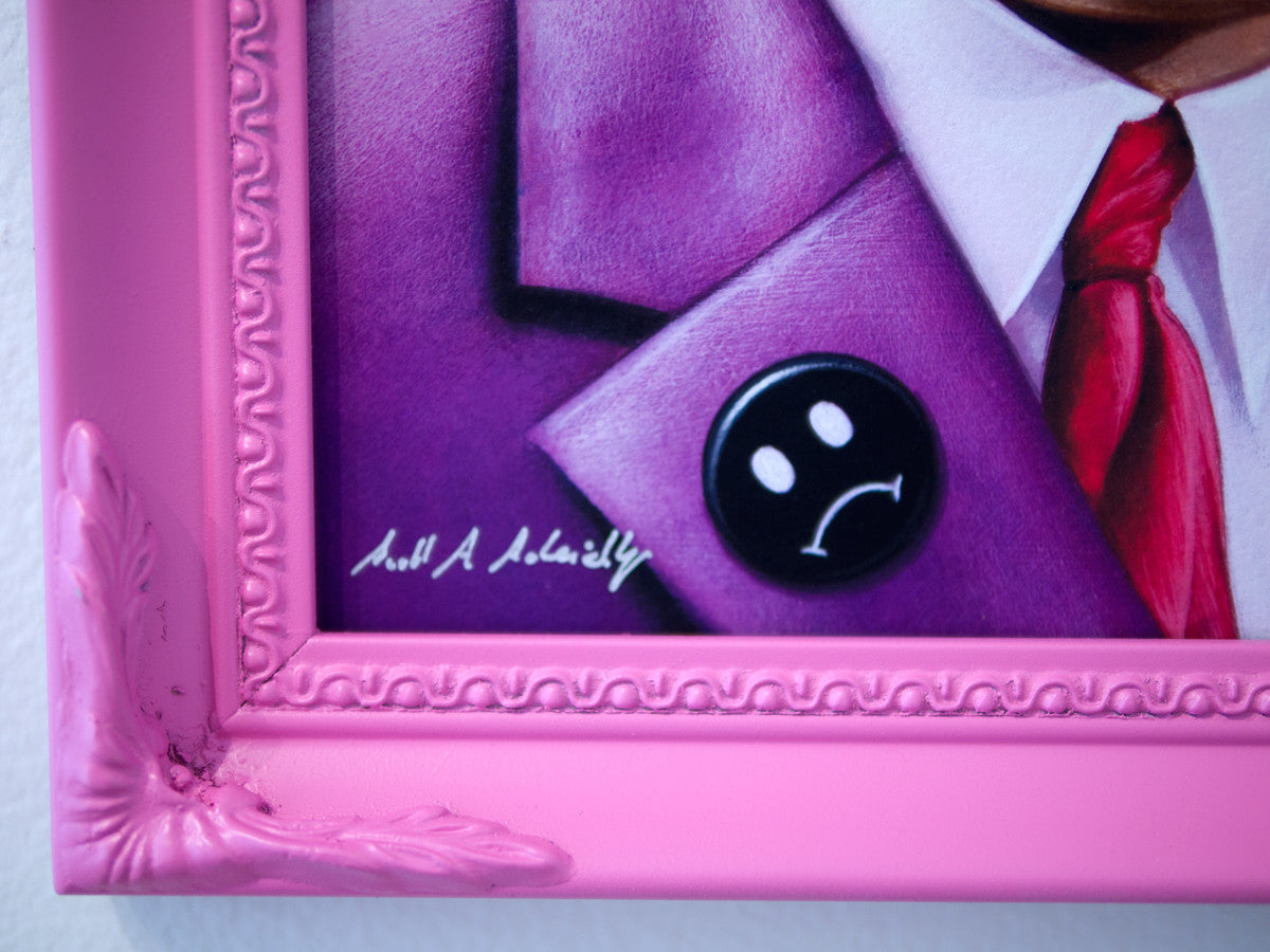 This limited edition framed image by Scott Scheidly showcases a person in a purple suit and a black button with a white sad face. The pink ornate frame, which is chipped at the corner, and the button are prominent features, along with the artist’s signature.