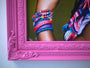 A vibrant Scott Scheidly archival pigment print features a person’s arm with colorful bracelets, including one saying LOVE, surrounded by brightly colored fabrics in a pink ornate frame.