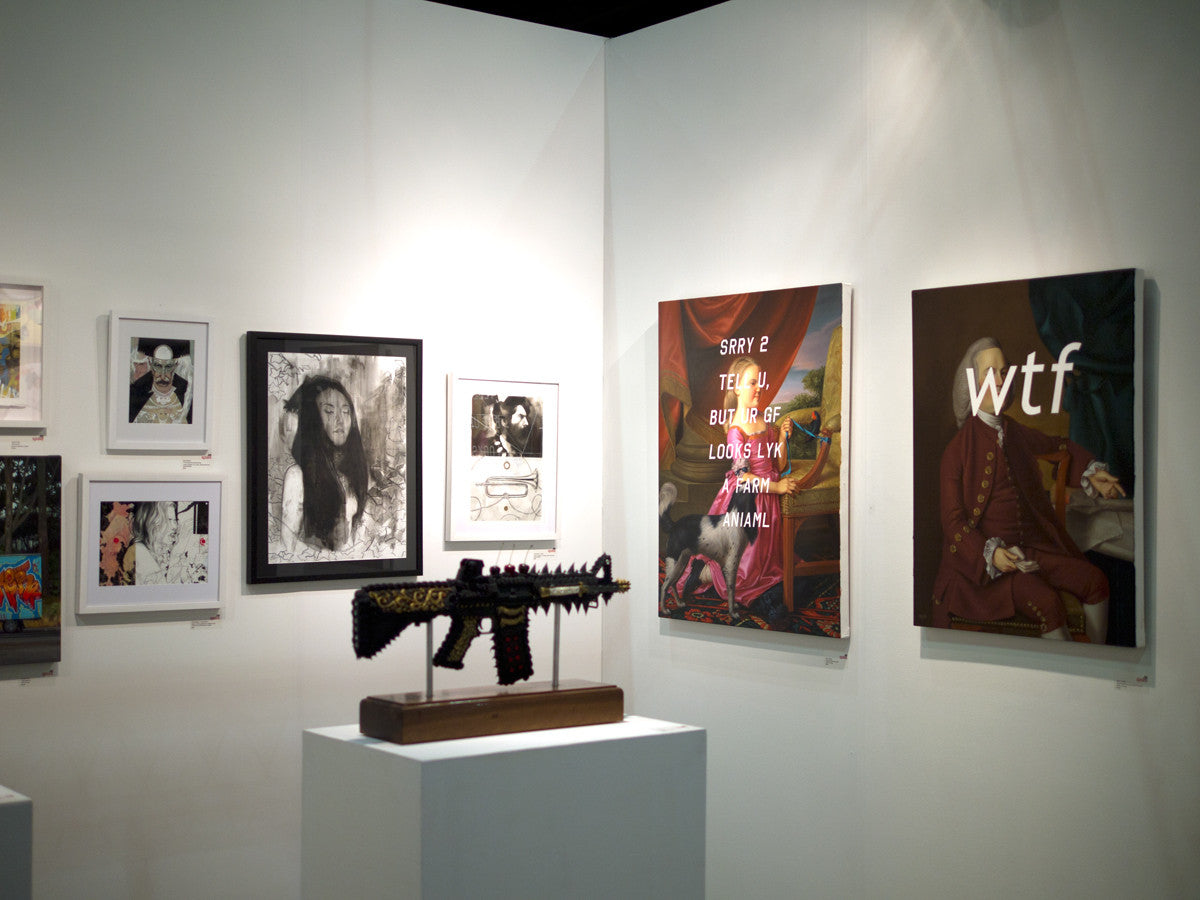 The gallery showcases portraits and abstract artworks on white walls, including Lotus Eater III by Nimit Malavia and an intriguing piece called art on mylar. A sculpted object resembling a weapon is artfully displayed on a pedestal.