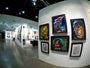 A gallery features vibrant artwork, like sci-fi and fantasy portraits. A standout is a striking Jason Edmiston piece—acrylic on wood panel—that captures attention. The polished concrete floor enhances the open, welcoming atmosphere.