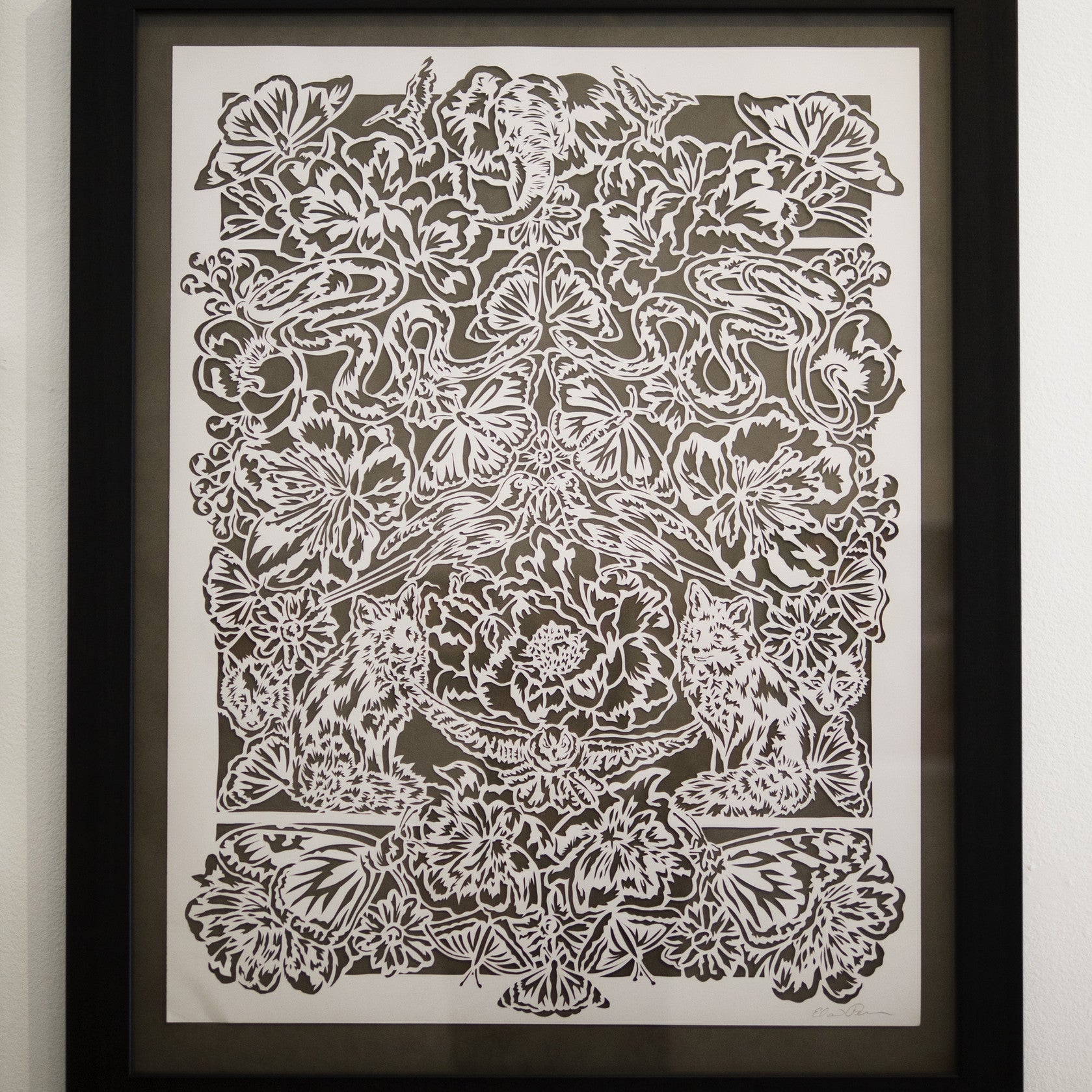 Elaine Penwells intricate white papercut art showcases symmetrical floral designs, animals, and butterflies, creating a harmonious and detailed menagerie against a dark background.