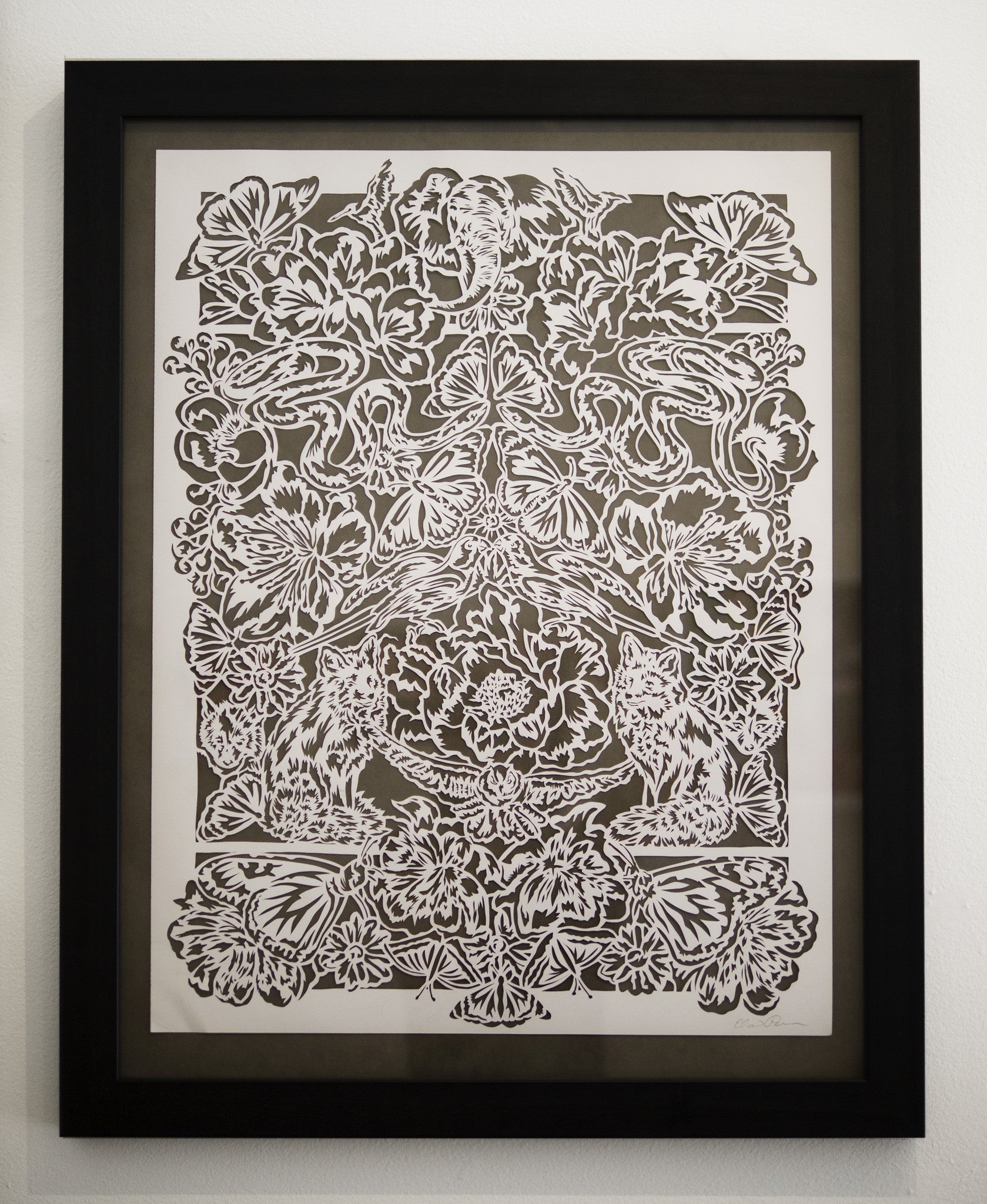 Elaine Penwells intricate white papercut art showcases symmetrical floral designs, animals, and butterflies, creating a harmonious and detailed menagerie against a dark background.