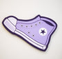 Illustration of Matt Ritchie’s purple high-top sneaker, similar to a classic Converse, with a black star on the side. It has white laces and stitching on a stark white background, with an outline evocative of hand-cut wood art detailed in bold black lines.
