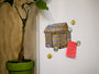 A small tree in a green pot sits by a white wall with a cartoon shed drawing. Scattered around are round magnets from Arthurs Plaid Pants Twin Peaks set, and theres also a pink sticky note with a to-do list.