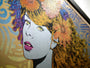 Close-up of a vibrant pop art painting by Chuck Sperry, inspired by Naiad. It showcases a womans face with colorful, flower-adorned hair flowing over an oak panel. Swirling patterns and contrasting hues in the background enhance this dynamic and expressive limited edition artwork.