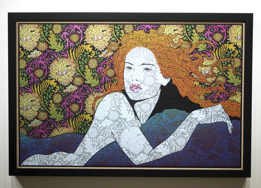 A captivating Chuck Sperry-inspired artwork showcases a red-haired woman lying on her side against a vibrant floral background. Her body and hair seamlessly merge with intricate patterns, creating a textured effect on an oak panel framed in black.