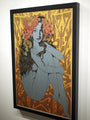 This framed artwork on an oak panel, branded Chuck Sperry, features Ariadne with long hair seated, arms wrapped around her knees. Her gray skin contrasts with her heads large orange and red flowers against a backdrop of abstract golden patterns.