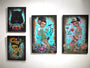 Four vibrant, surreal paintings by Caia Koopman adorn the white wall. Each acrylic on wood panel piece showcases stylized figures, a black wolf, flowers, and abstract elements in vivid turquoise and pink hues. These artworks each convey unique and imaginative themes.