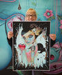A woman with glasses holds a vibrant Caia Koopman limited-edition painting. It features a stylized female figure with a heart amid ornate floral elements, set against an artistic background bursting with flowers and abstract designs in this stunning archival pigment print.