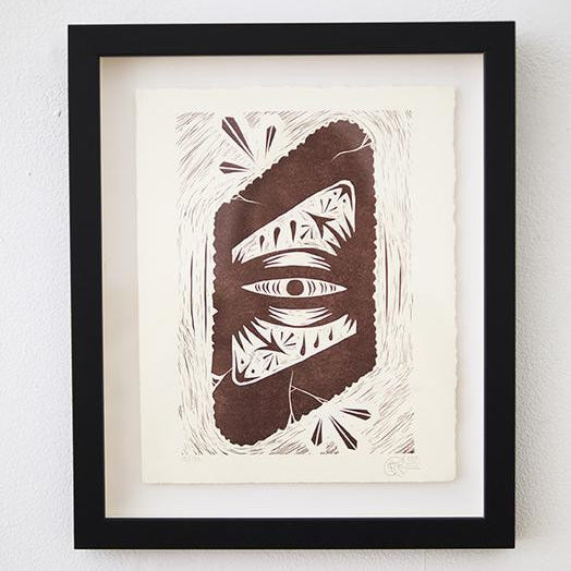 Framed artwork by GATS showcasing Infinite Eye, an abstract eye design in brown tones with geometric patterns on white paper. This letterpress linoleum cut is part of a signed and numbered edition, elegantly displayed against a plain white wall.