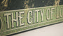 Close-up of a vintage-style screen print poster by Godmachine, featuring green and yellow textures. The text reads THE CITY OF LOS... with some letters hidden, capturing the mystery of a Roxie Theater classic. Its distressed appearance enhances the enigmatic design.