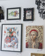 A gallery wall at Spoke Art features diverse artworks: a colorful abstract fish, a Joshua Budich-framed wolf, a geometric print of two people, a striking portrait of a woman with red halo, and other decorative pieces inspired by Lord of the Thrones.