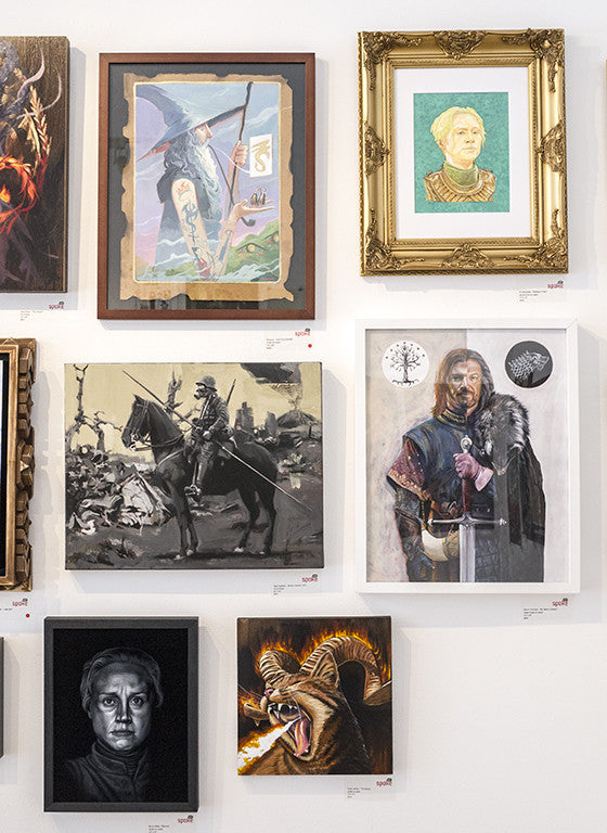 A PJ McQuade wall display features framed artwork: a wizard, medieval warriors inspired by George R.R. Martin, a Brienne of Tarth lookalike, a stern face, and a fire-breathing creature; frames ranging from simple to ornate.