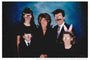 This Rezatron family portrait for Gallery1988s art show showcases five formally dressed figures with exaggerated cartoon eyes and round glasses, one of whom wears pink bunny ears. The whimsical scene unfolds against a blue gradient background.