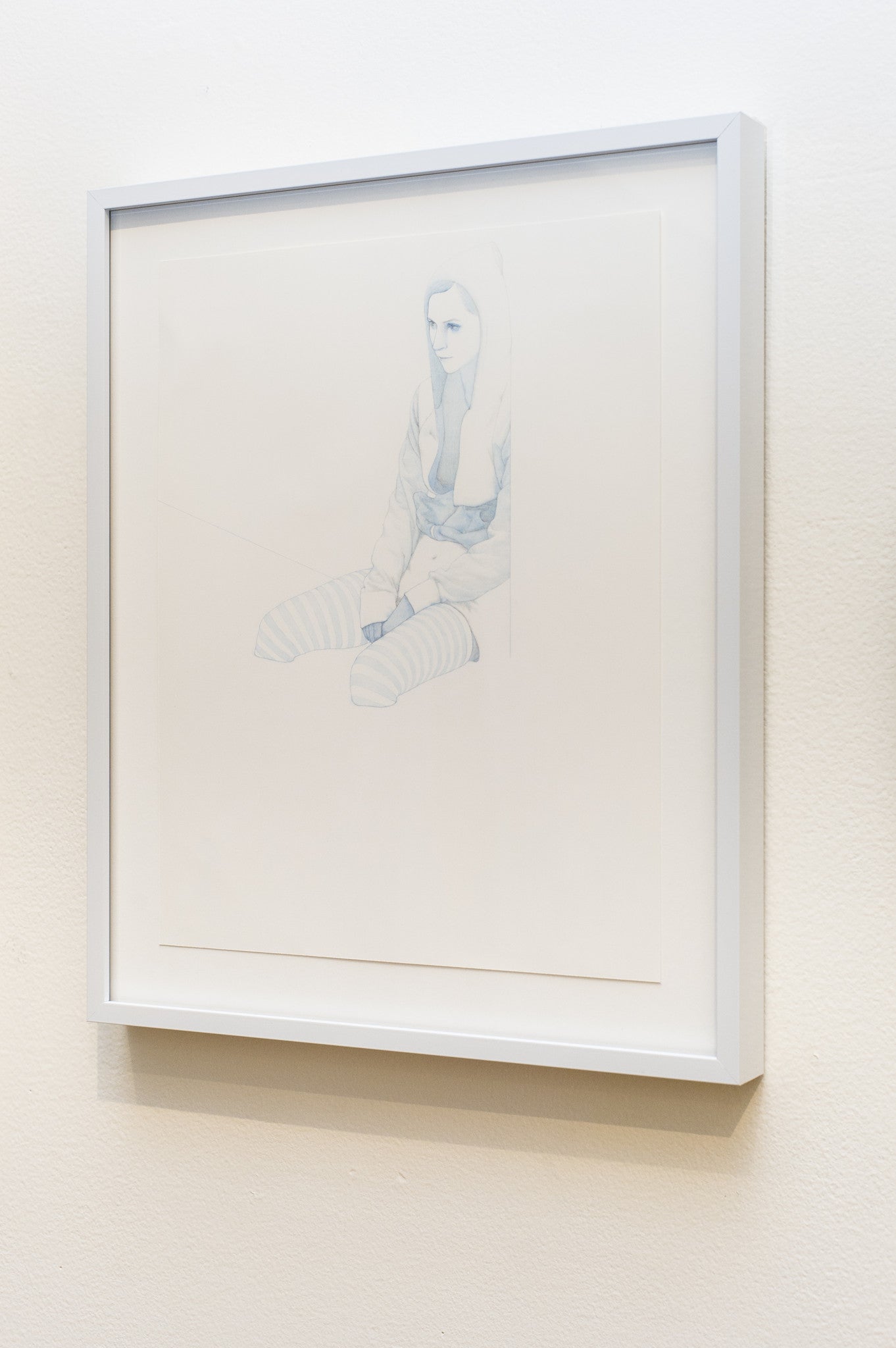A framed Steve Kim artwork on the wall depicts a person with long hair, wearing a hoodie and striped socks. The image has a light, sketch-like quality with colored pencils, showcasing minimal color for understated elegance.